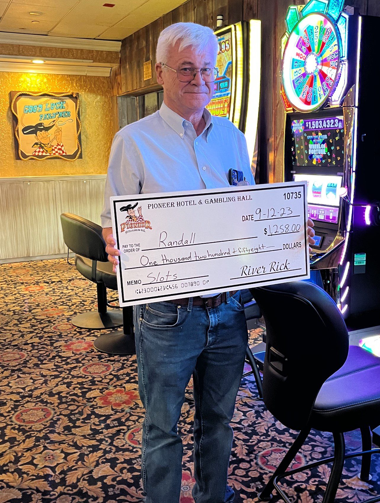 67c0c5d379aae_Pioneer Winnings A man holding up a large check in front of a slot machine.